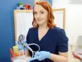 Kobieta w niebieskim fartuchu trzyma model ucha, pokazując jego budowę, w tym ślimak, który przypomina kształtem nerw słuchowy.