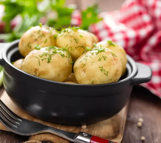 Gotujesz ziemniaki na ból ucha? Te młode ziemniaczki, posypane koperkiem, wyglądają apetycznie. Obok widelec i czerwono-biała serwetka.
